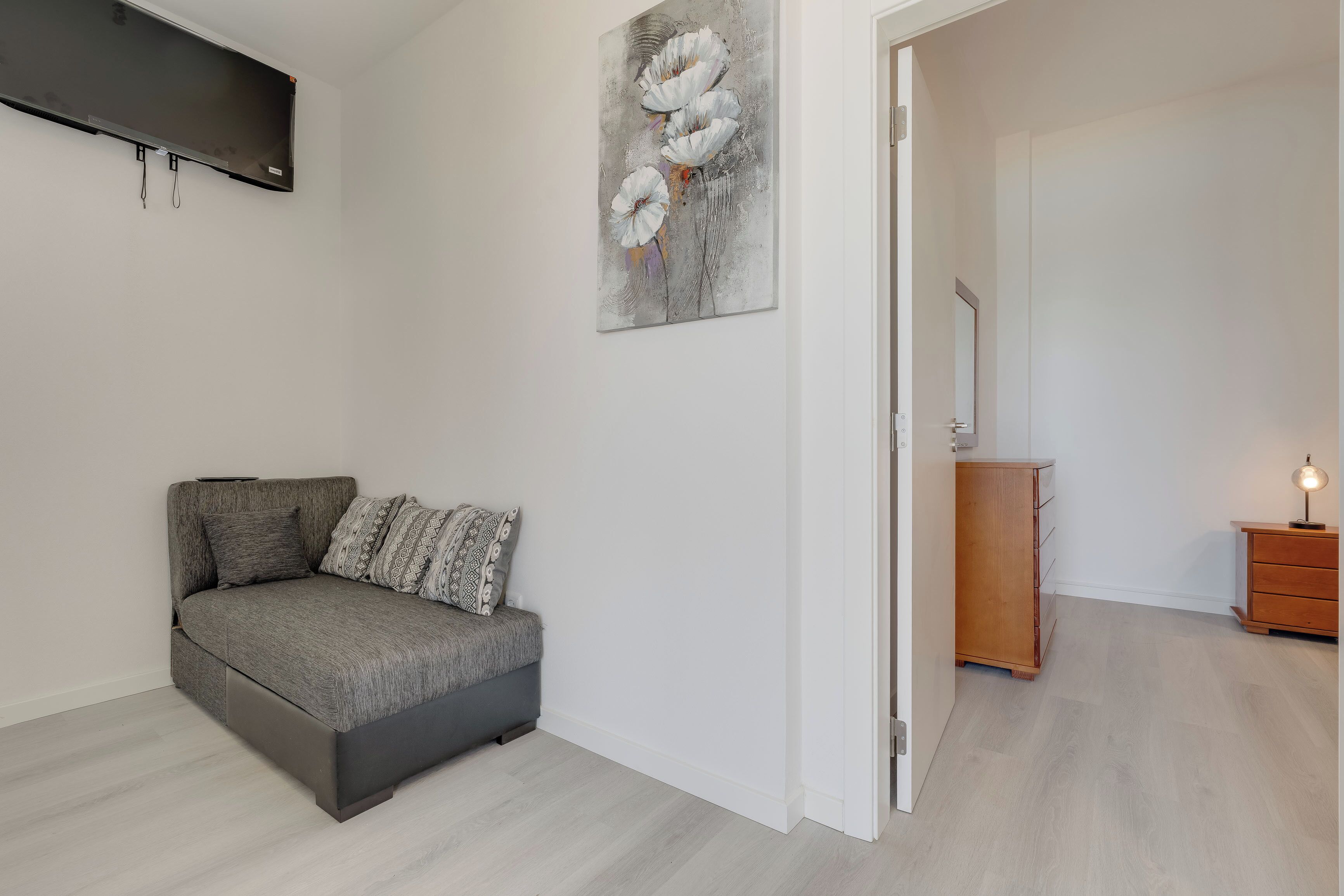 Un dormitorio moderno con un sofá gris, un cuadro, un armario de madera y una mesita de noche.