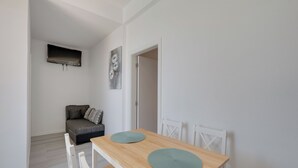A dining area with a wooden table, two white chairs, and a grey sofa with pillows.