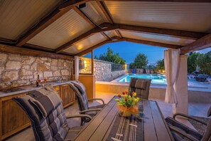 An outdoor kitchen with stone walls, a pool, and a covered seating area. - Holiday House Nives with pool and playground (Orihi)