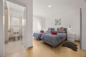A bedroom with two beds, a nightstand, a bathroom with a toilet and sink, and a large window. - Holiday House Nives with pool and playground (Orihi)