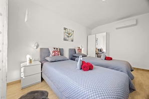 A bedroom with two beds, a nightstand, a mirror, and a wall-mounted air conditioner. - Holiday House Nives with pool and playground (Orihi)