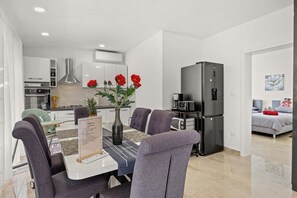 A modern kitchen with white cabinets, a stainless steel refrigerator, and a dining area with a table and chairs. - Holiday House Nives with pool and playground (Orihi)