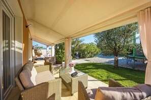 A covered patio area with wicker furniture, a table with a vase, and a view of the outdoors. - Holiday House Nives with pool and playground (Orihi)