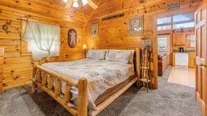 A wooden cabin interior with a bed, a ceiling fan, a kitchen area, and a sign reading "My favorite place is where you find your home." - Dog Friendly Cabin, Sleeps 2・Hot Tub・Near Park (Pigeon Forge)