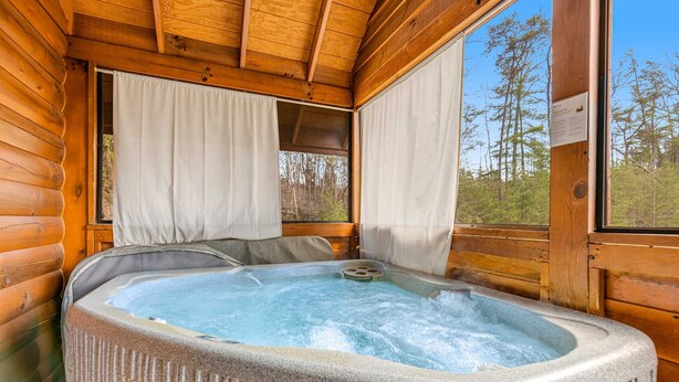A hot tub in a log cabin with a view of the forest through large windows. - Dog Friendly Cabin, Sleeps 2・Hot Tub・Near Park (Pigeon Forge)