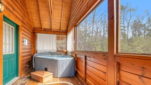 A log cabin with a hot tub, wooden floors, and a large window offering a forest view. - Dog Friendly Cabin, Sleeps 2・Hot Tub・Near Park (Pigeon Forge)