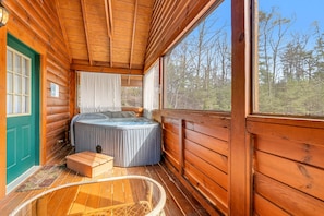 A log cabin with a hot tub, wooden floors, and a large window offering a forest view. - Dog Friendly Cabin, Sleeps 2・Hot Tub・Near Park (Pigeon Forge)