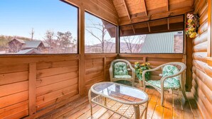 A wooden cabin with a balcony, wicker chairs, a glass table, and a view of the surrounding area. - Dog Friendly Cabin, Sleeps 2・Hot Tub・Near Park (Pigeon Forge)