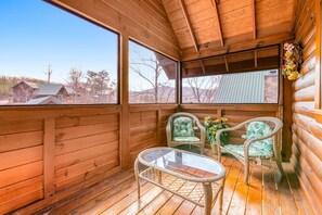 A wooden cabin with a balcony, wicker chairs, a glass table, and a view of the surrounding area. - Dog Friendly Cabin, Sleeps 2・Hot Tub・Near Park (Pigeon Forge)