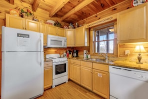 Cocina compacta con armarios de madera, un refrigerador, un microondas, una estufa y un lavamanos.