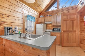 Eine Holzhüttenküche mit Granitarbeitsplatte, einem weißen Kühlschrank, Herd und Holzschränken.