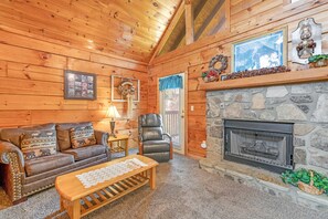 Ein gemütliches Blockhaus mit Kamin aus Stein, Holzwänden, einer Ledersofa und einem Kissen mit Karomuster.