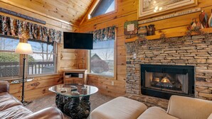 A cozy cabin interior with a stone fireplace, wooden walls, a flat-screen TV, and a comfortable seating area. - Serene Cabin・07 mi. from Pigeon Forge・Hot Tub・Pool (Pigeon Forge)