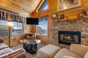 A cozy cabin interior with a stone fireplace, wooden walls, a flat-screen TV, and a comfortable seating area. - Serene Cabin・07 mi. from Pigeon Forge・Hot Tub・Pool (Pigeon Forge)