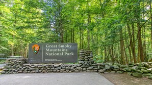 A sign for Great Smoky Mountains National Park with a stone wall and forested background. - Serene Cabin・07 mi. from Pigeon Forge・Hot Tub・Pool (Pigeon Forge)