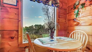 A wooden interior with a round table and two chairs, a window with a view of trees, and a decorative sign on the wall. - Serene Cabin・07 mi. from Pigeon Forge・Hot Tub・Pool (Pigeon Forge)
