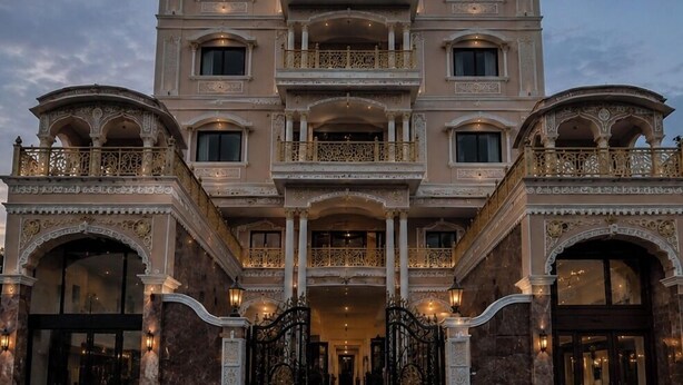 Un edificio de varios pisos con balcones ornamentales, amplias puertas arqueadas y una entrada imponente.