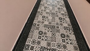 Un pasillo con suelo estampado, obras de arte enmarcadas en las paredes y una silla roja al fondo.