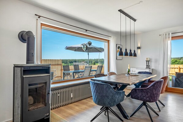 A modern dining area with a large table, chairs, and a view through a large window.