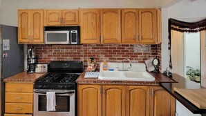 A kitchen with wooden cabinets, a microwave, a stove, a sink, and a brick backsplash.