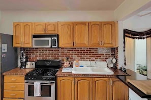 A kitchen with wooden cabinets, a microwave, a stove, a sink, and a brick backsplash. - Maison de sirènes 2, Bohemian, ecclectic apartment (Brooklyn)