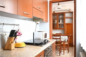 A kitchen with wooden cabinets, a microwave, a stove, and a dining area with a table and chairs. - SE283 – Senigallia, four-room apartment with private parking space and balcony (Senigallia)