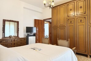 Ein Hotelzimmer mit Bett, Schminktisch, Fernseher, Kleiderschrank und einer Chandelier.