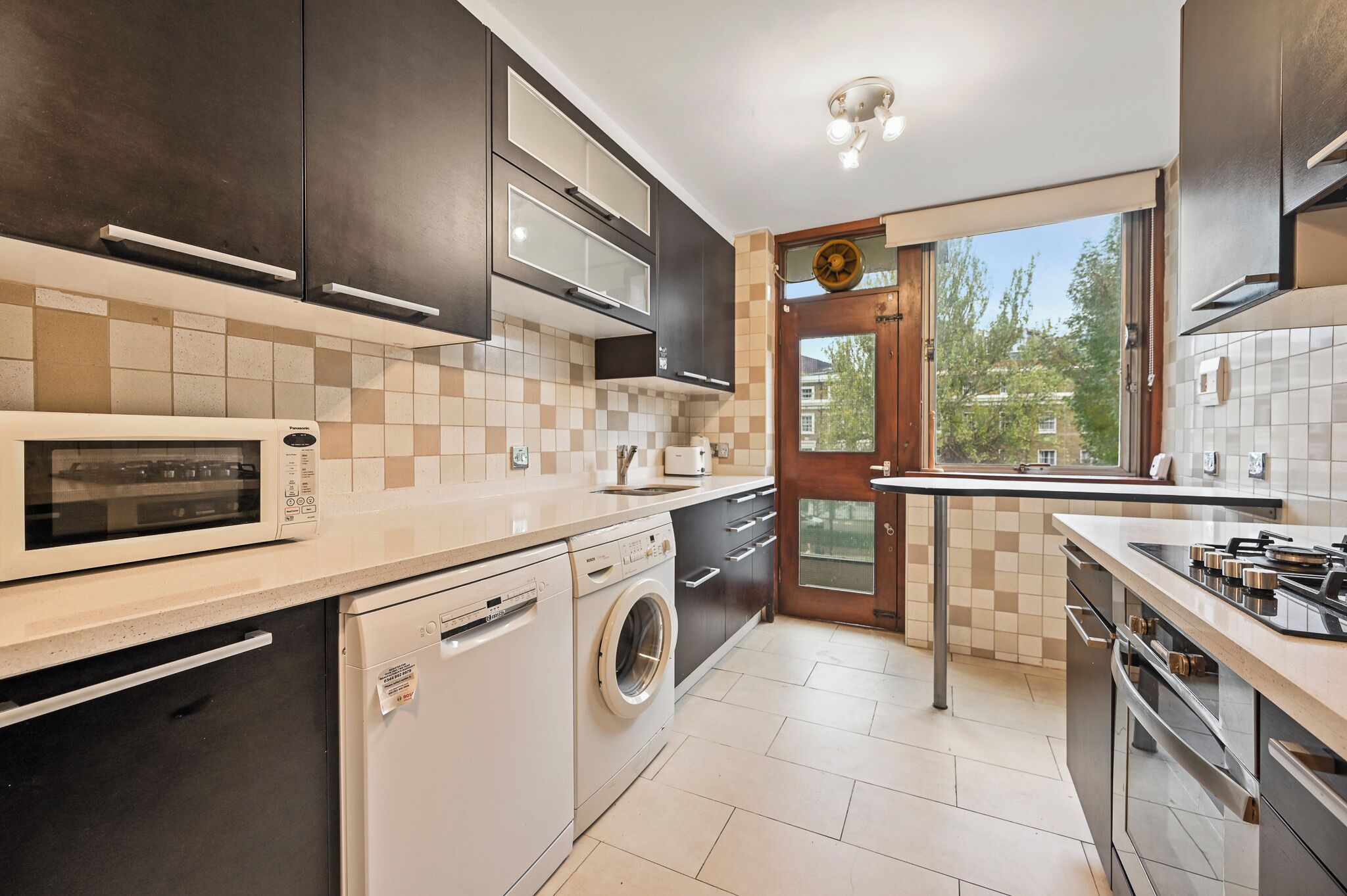 A modern kitchen with a dishwasher, washing machine, microwave, and stove.
