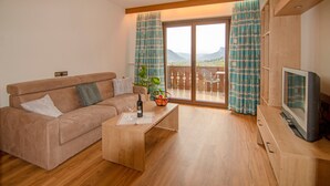 Ein Wohnzimmer mit Sofa, Couchtisch, Fernseher und einem Balkon mit Vorhängen.