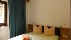 Ein Hotelzimmer mit einem Bett, zwei Kissen, einem Nachttisch, einer Lampe und einem Fenster mit Vorhängen.