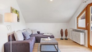 A modern living room with a sectional sofa, a coffee table, a lamp, a radiator, and a window with a view. - Dog-friendly, modern holiday apartments with terrace, 2 balconies and Wi-Fi (Bräunlingen)