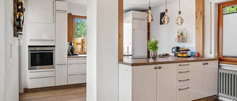 Una cocina moderna con armarios blancos, horno integrado y encimera de madera.