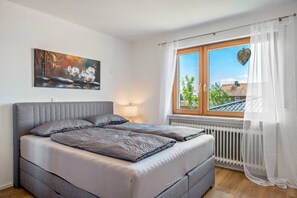Een slaapkamer met een bed, nachtkastje, lamp, raam met gordijnen en een schilderij aan de muur.