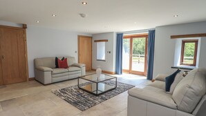 A spacious living room with a sofa, a glass coffee table, and a large sliding glass door leading to a balcony. - Dam House Barn (Settle)