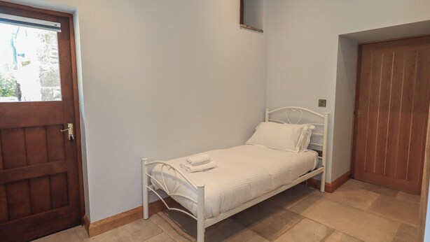 A small, single-bed room with a wooden door and a window. - Dam House Barn (Settle)