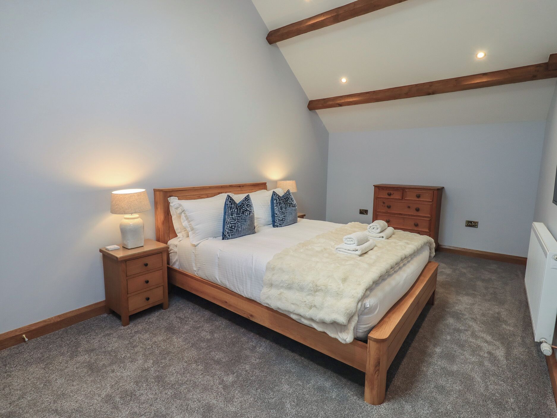A bedroom with a wooden bed, two bedside tables, a dresser, and a radiator.