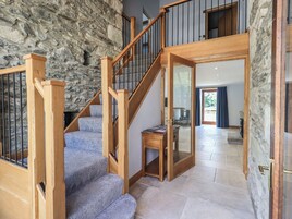 Una escalera con barandillas de madera y paredes de piedra que lleva a una habitación con vistas al exterior.