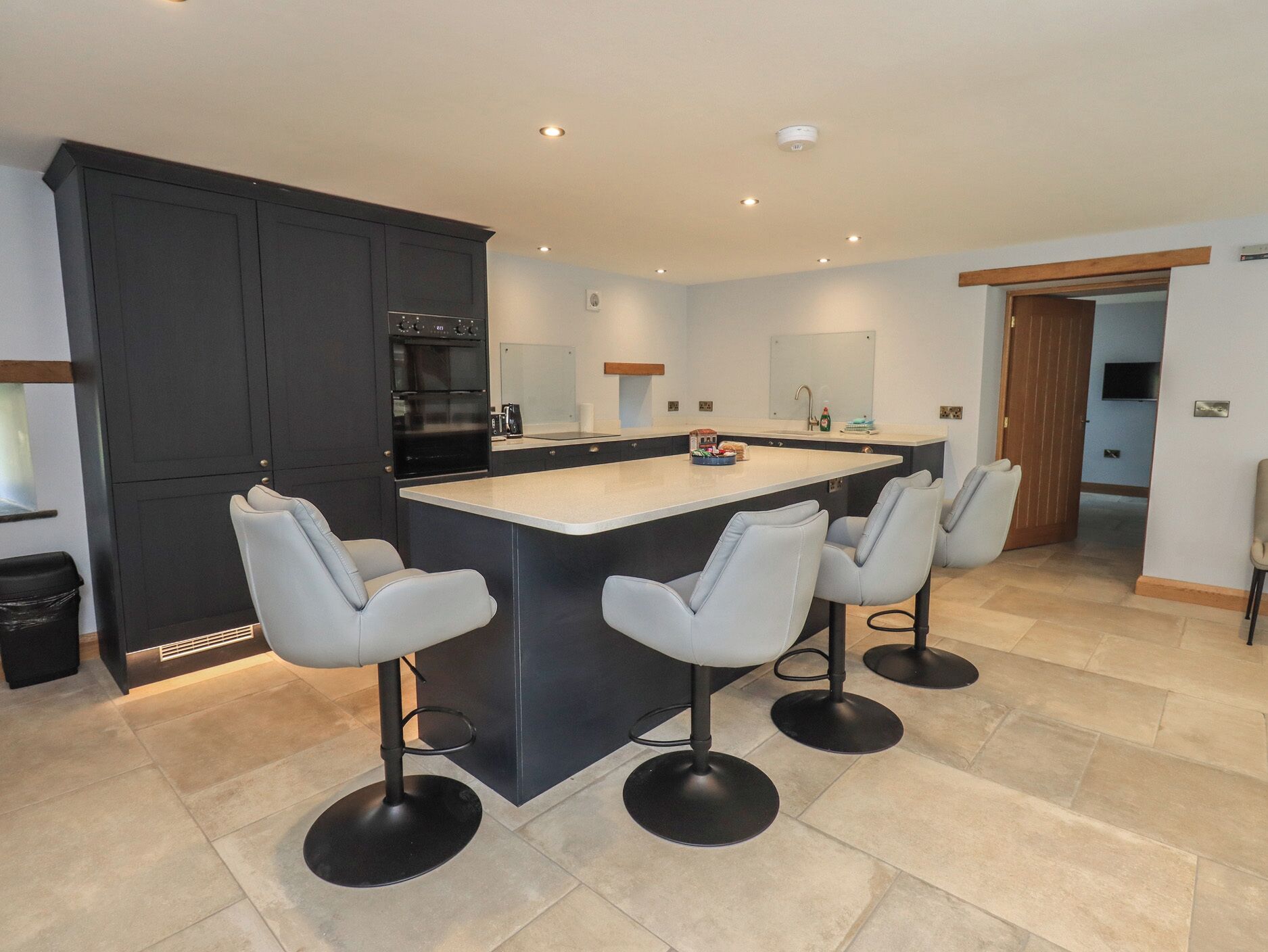 A modern kitchen with a central island, bar stools, dark cabinetry, and a built-in oven.