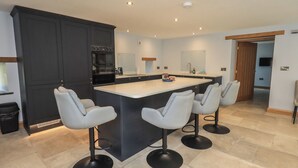 A modern kitchen with a central island, bar stools, dark cabinetry, and a built-in oven. - Dam House Barn (Settle)