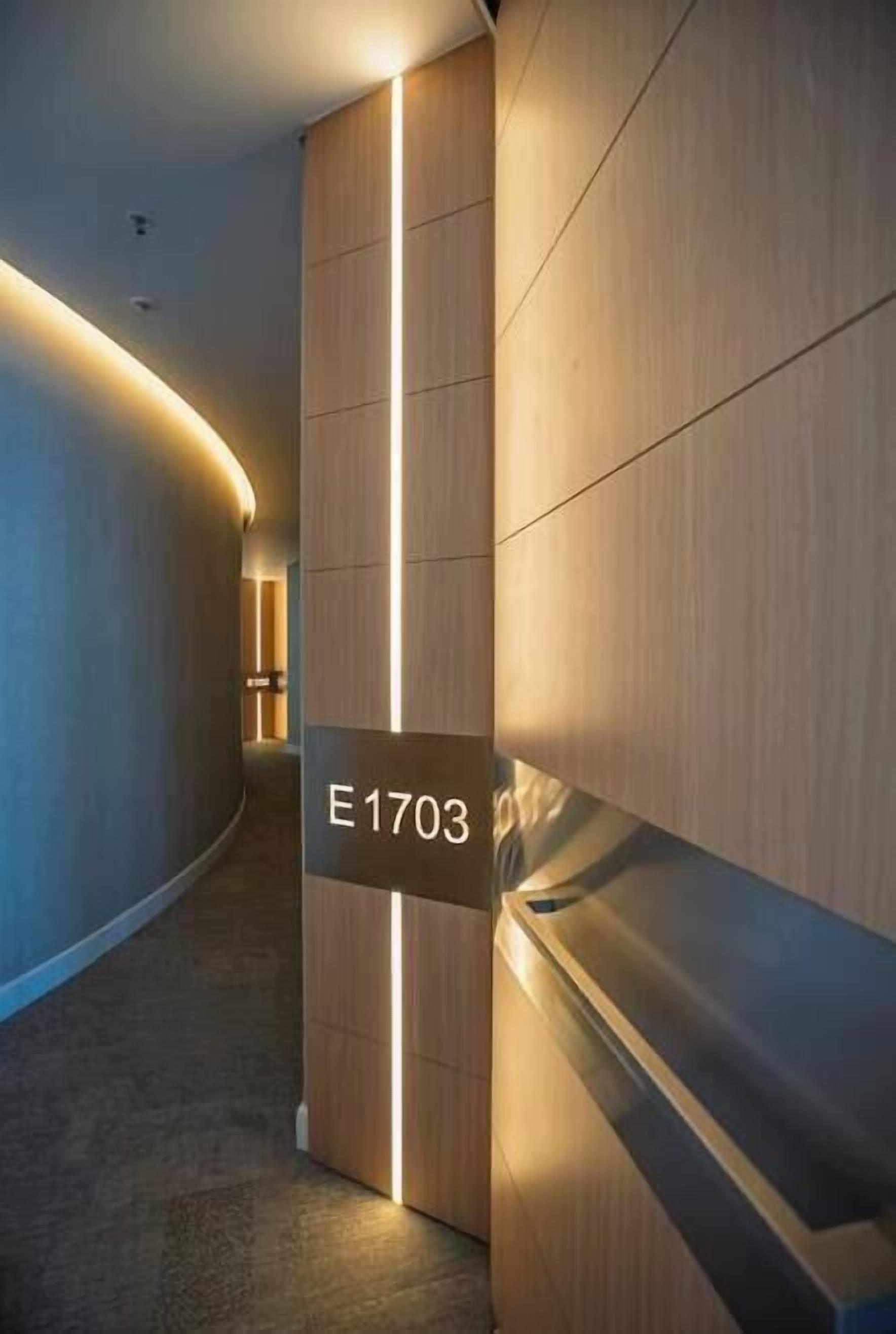 Un couloir avec une plaque indiquant « E1703 », un mur en bois et une bande lumineuse.