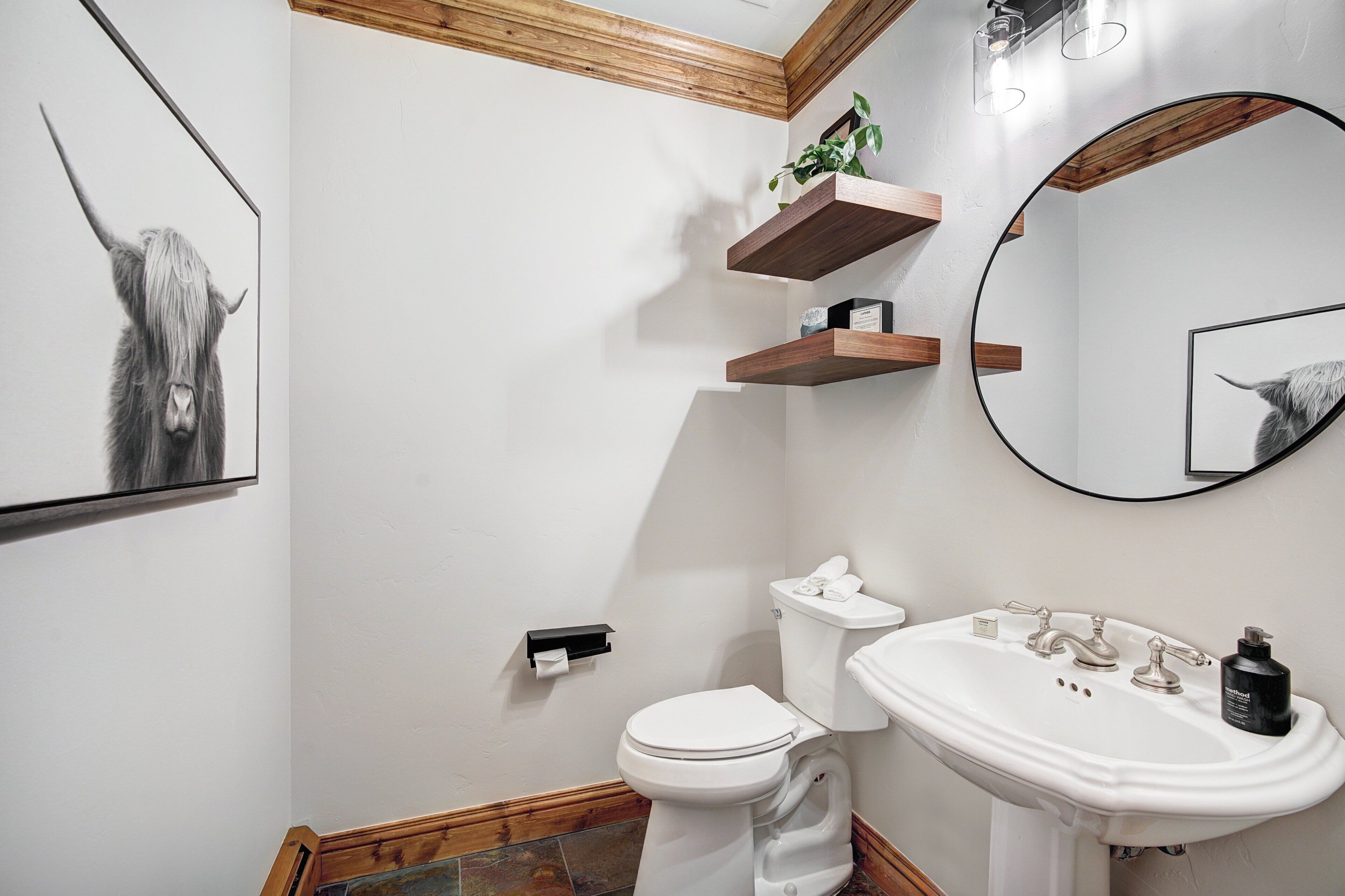 A bathroom with a toilet, sink, wooden shelves, and a mirror.