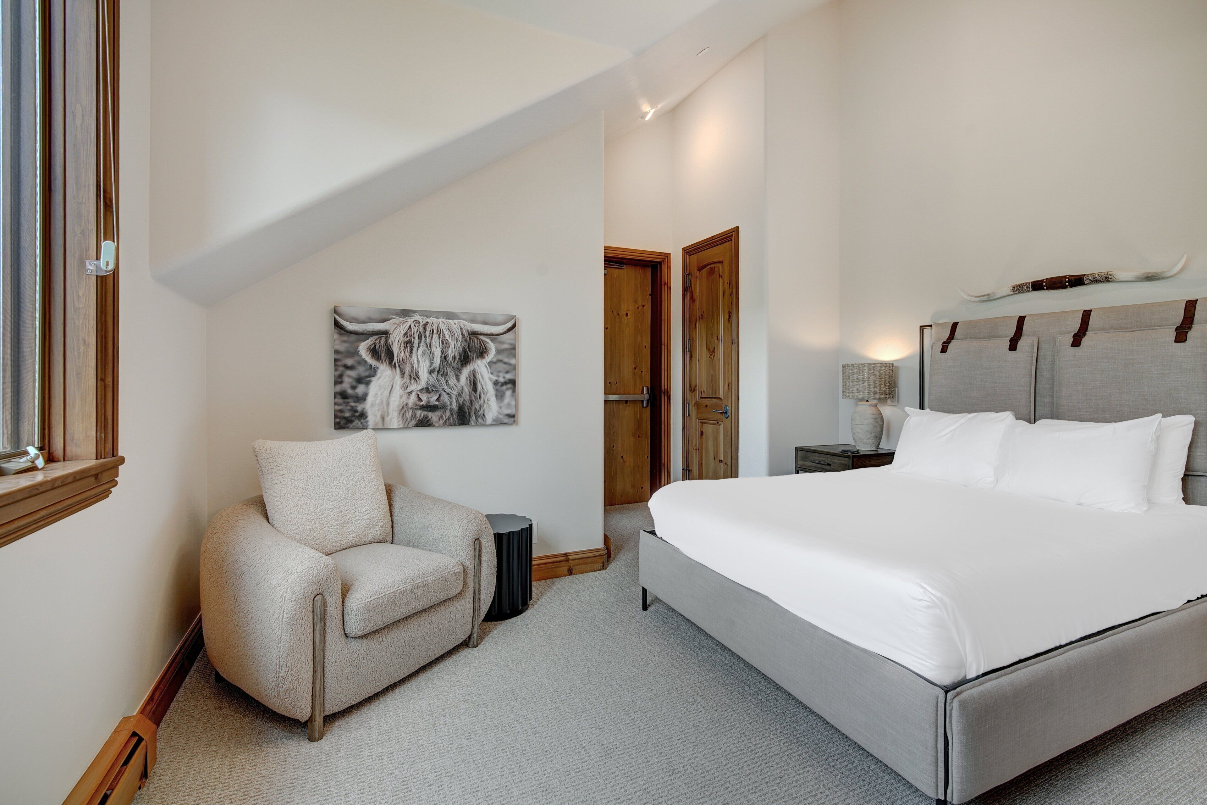 Een slaapkamer met een groot bed, een stoel, een nachtkastje, een lamp en een deur.
