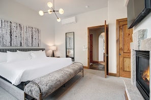 Ein modernes Schlafzimmer mit einem großen Bett, einer Bank, einem Kamin und einem zur anderen Kammer führenden Gang.