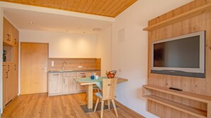 Een moderne keuken met houten kasten, een eettafel met stoelen en een aan de muur bevestigde televisie.