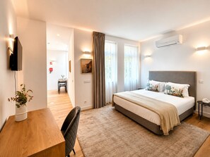 Una camera d'albergo moderna con un letto grande, una scrivania e una sedia. Sono presenti due finestre con tende, un condizionatore d'aria e un televisore a parete.
