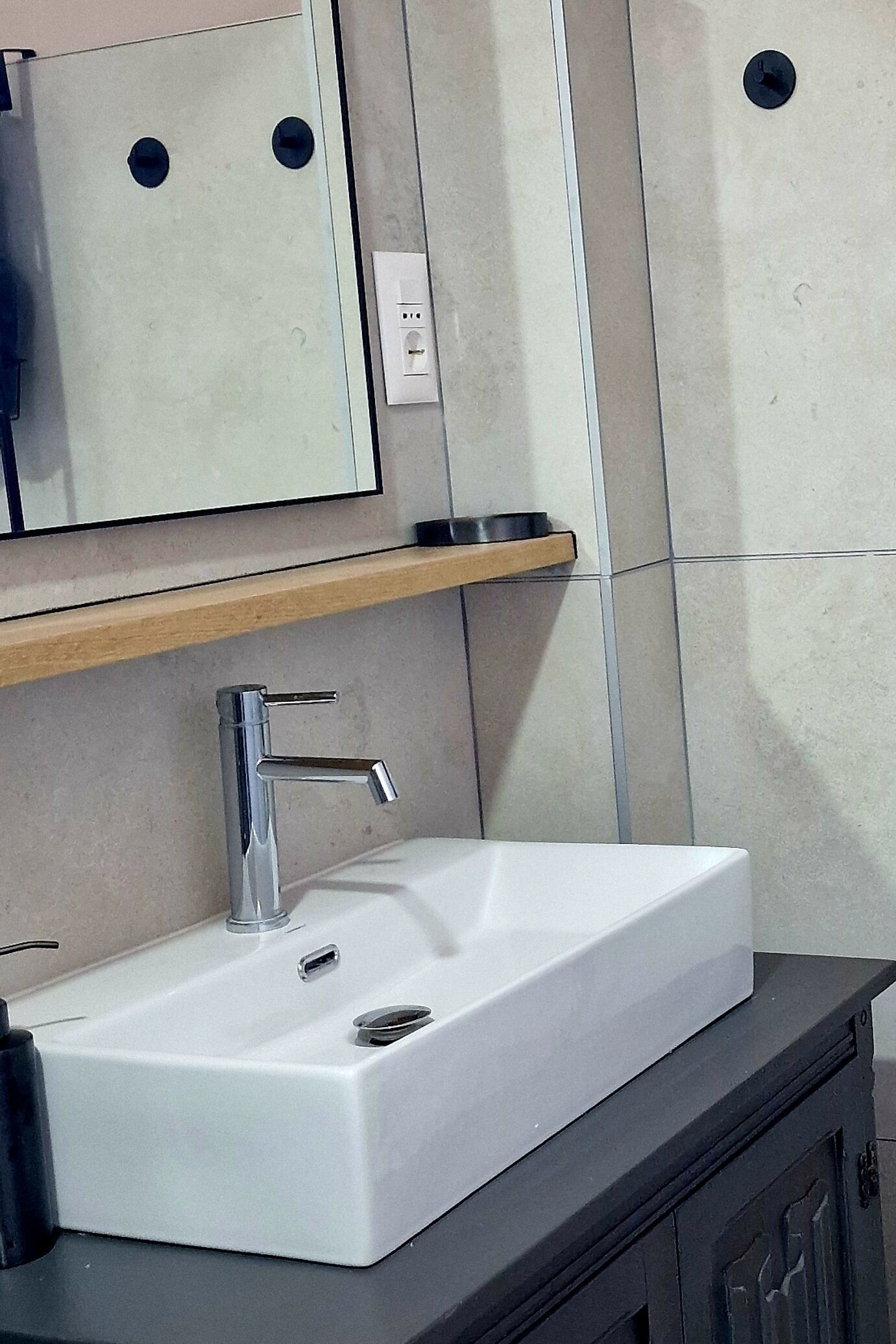 A bathroom with a white sink, a mirror, and a wooden shelf.