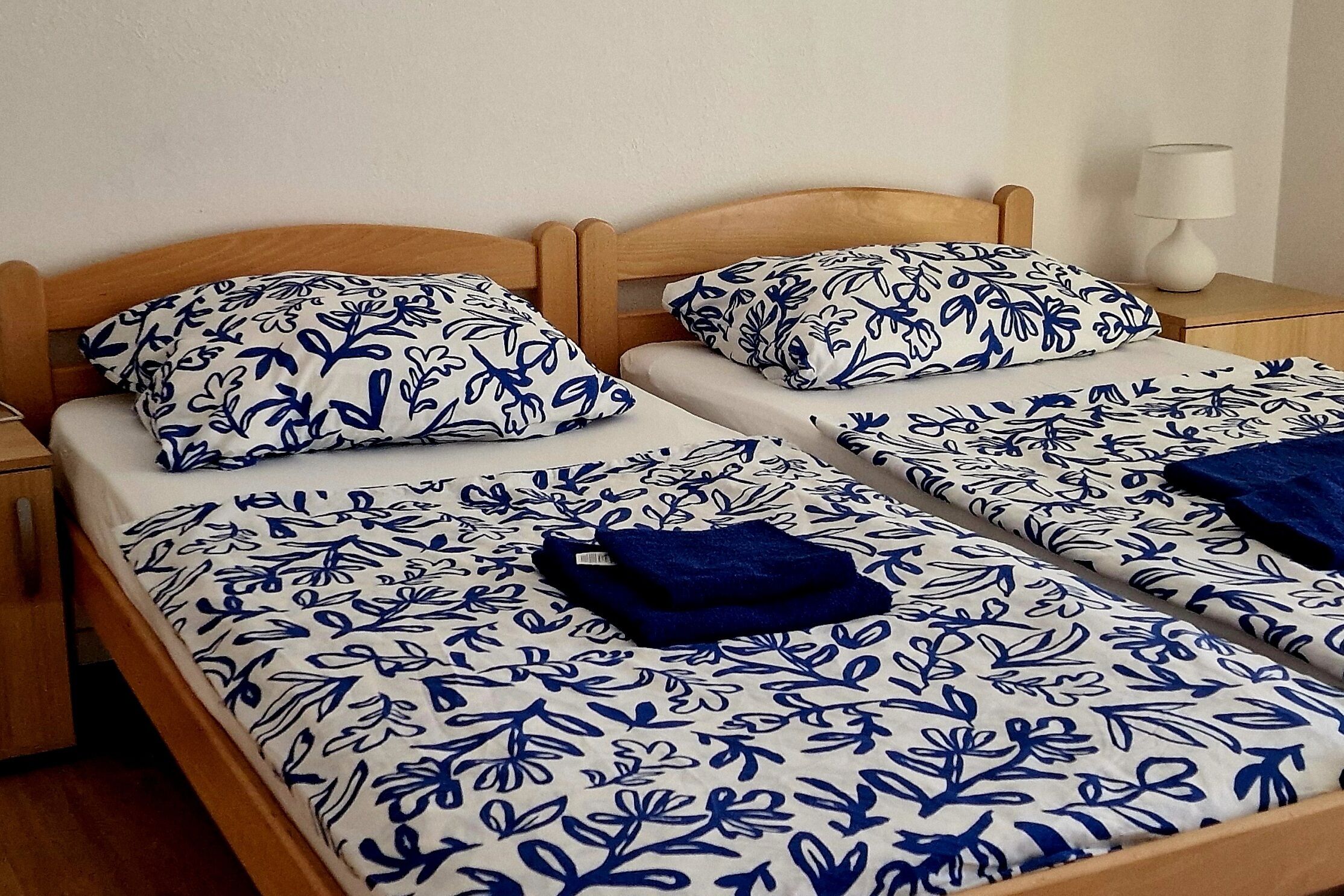 Ein Doppelbett mit blumigem Bettzeug und Kissen, ein hölzernes Kopfteil, ein Nachttisch mit Lampe und ein Beistelltisch.