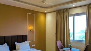A hotel room with a bed, a desk with chairs, a ceiling fan, and a window with curtains.