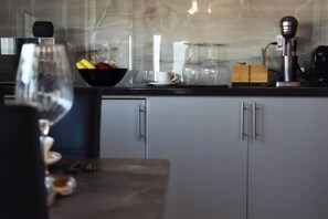 A kitchen with a glass bowl of fruit, a coffee maker, and a wine glass. - Elysian Blue (Petalidi)