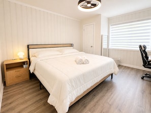 A neatly made bed with a headboard, a bedside table with a lamp, a chair, and a window with blinds. - Stylish & Modern 2BR Suite -Private Entry - Prime Location (Atlanta)